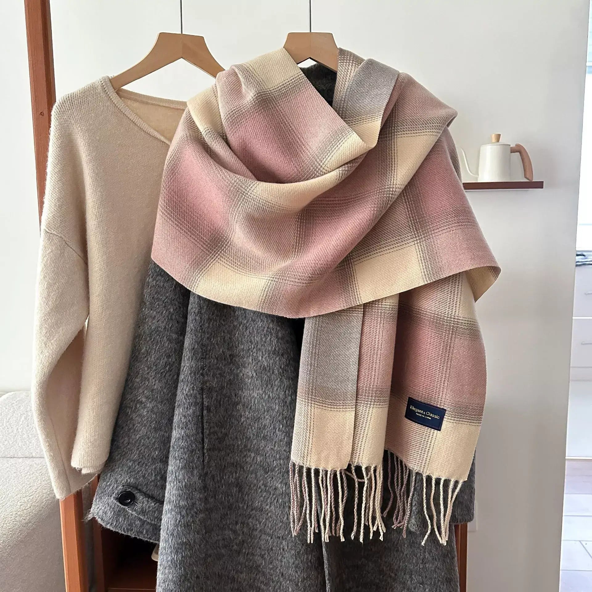 plaid fringe scarf in soft pink and beige, draped over gray coat on hanger, polyester one-piece imported