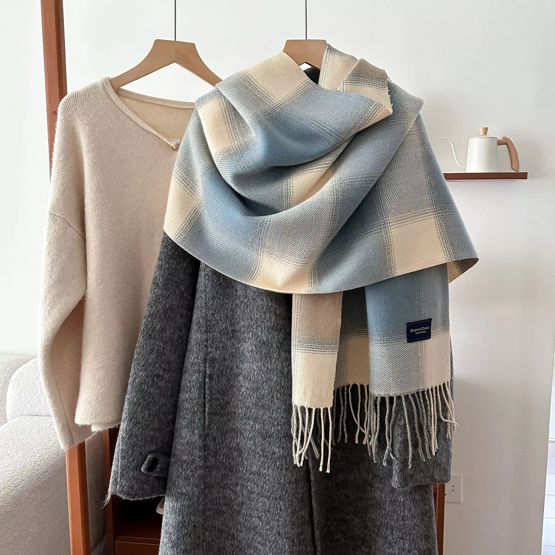 Alt Tag: plaid fringe scarf in blue and cream plaid pattern with tassel fringe, styled over gray wool coat on hanger Main image