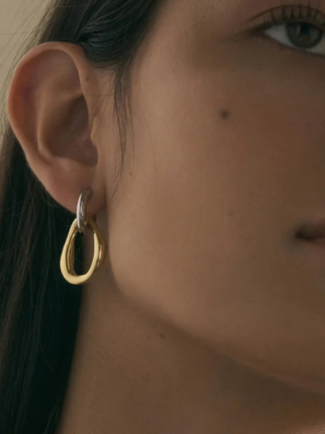 Close-up of 18K gold-plated asymmetrical earrings on a woman. Hauptbild